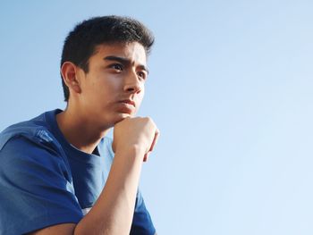 Low angle view of boy with hand on chin against clear sky
