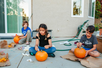 Two sisters and brother carve pumpkins outside