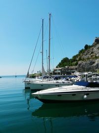 Boats moored at harbor against clear blue sky