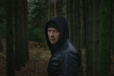 Portrait of man standing by tree trunk in forest