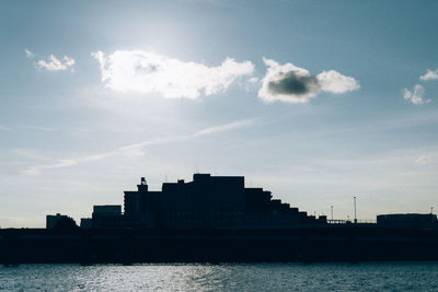 Silhouette buildings by sea against sky