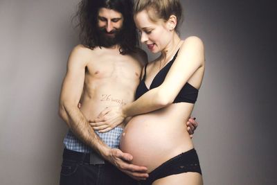 Shirtless with pregnant woman standing against gray background