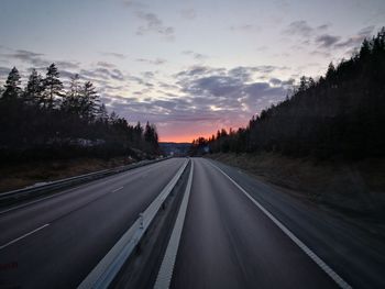 Road amidst trees against sky during sunset