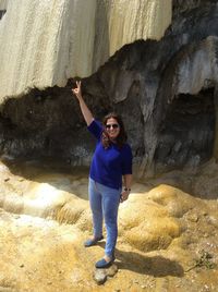 Portrait of woman wearing sunglasses with hand raised standing on rock