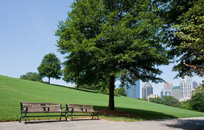 Park bench on field by building against clear sky