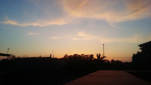 Road by silhouette trees against sky during sunset