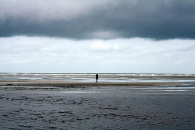 View of calm beach against cloudy sky