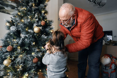 Grandparents decorate the christmas tree with their little granddaughter