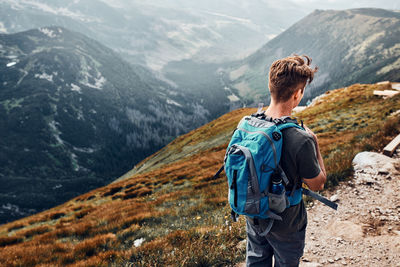 Young man with backpack hiking in a mountains, actively spending summer vacation