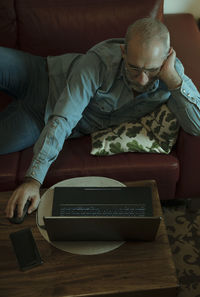 Portrait of adult man lying on sofa at home and using laptop