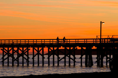 Silhouette bridge over sea against sky during sunset