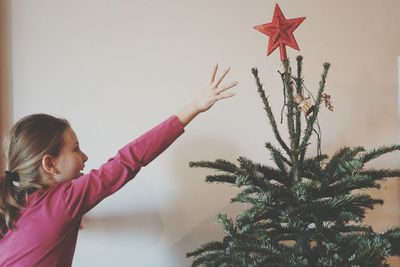 Girl reaching towards star on christmas tree at home