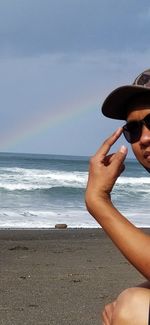 Midsection of man wearing sunglasses at beach against sky