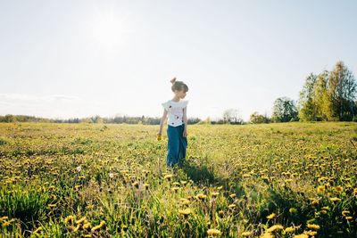 Girl walking through a yellow flower field with flowers in her hand