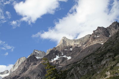 Low angle view of rocky mountains against cloudy sky on sunny day