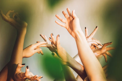 Cropped hands of female friends with arms raised against wall
