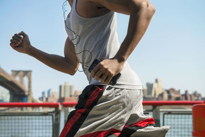 Midsection of man holding smart phone and jogging against sky