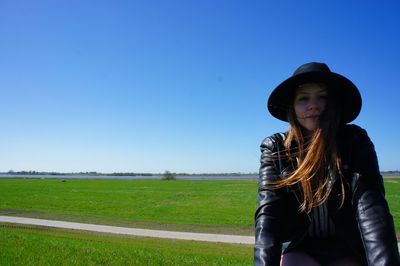 Portrait of man wearing hat standing on field against clear sky