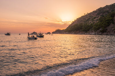 Boats moored in sea against sky during sunset