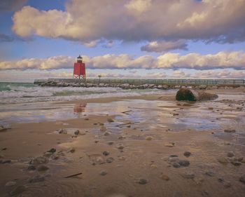 Lighthouse on beach against sky during sunset