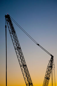 Low angle view of silhouette cranes against clear sky