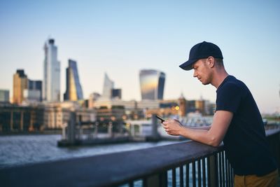 Side view of young man using smart phone against sky