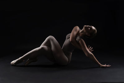 Ballet dancer stretching exercising against black background