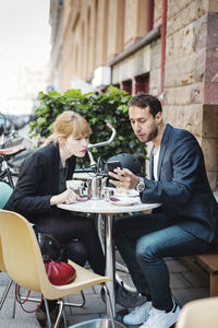 Business commuters using smart phone at sidewalk cafe