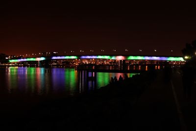 Illuminated city by river against sky at night