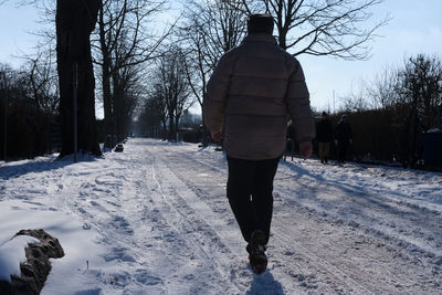 Rear view of man walking on snow covered footpath