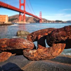 Close-up of old rusted chain with bridge in background