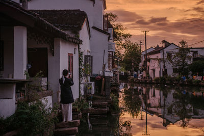 Rear view of woman walking on street against sky during sunset