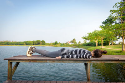 Man relaxing by lake against clear sky
