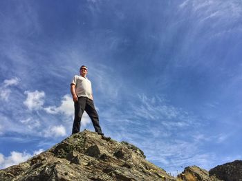 Low angle view of man standing on rock formation against blue sky