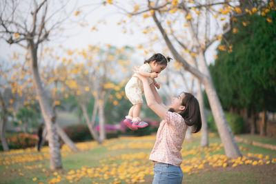 Side view of mother picking up daughter while standing in park