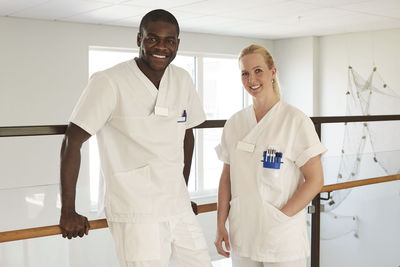 Portrait of confident male and female nurses standing against railing at hospital corridor
