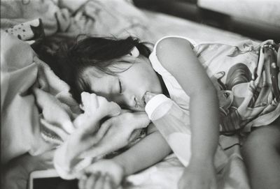 High angle view of girl with milk bottle sleeping on bed