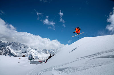 Professional athlete young male skier in an orange ski suit flies over the mountains after jumping