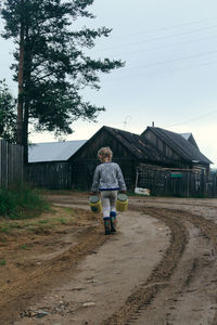 Rear view of woman walking on dirt road by building against sky