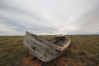 Abandoned boat on field by sea against sky