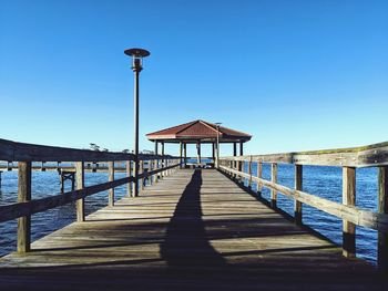 Pier on sea against clear blue sky