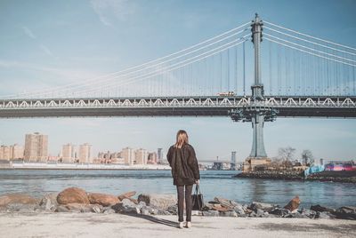 Woman standing on bridge over river with city in background