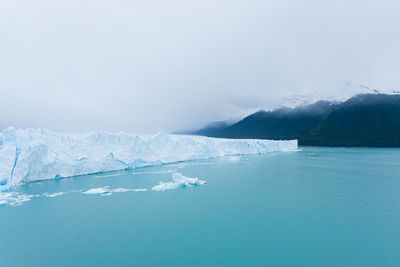 Scenic view of sea by snowcapped mountains against sky