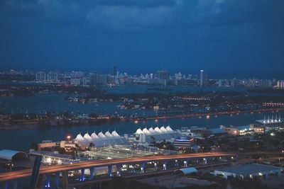 Illuminated cityscape by river against sky