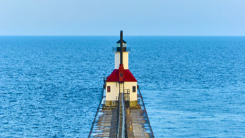 Lighthouse by sea against clear sky