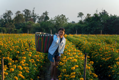 Contemplating woman standing amidst flowering plant with basket against clear sky