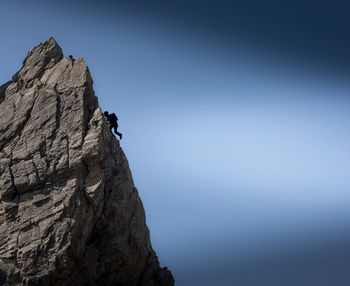 Low angle view of silhouette man climbing mountain against clear blue sky