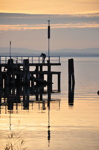 Wooden posts in sea against sky during sunset