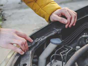 Hands of a young caucasian guy in a yellow jacket inspects an internal breakdown with an open hood