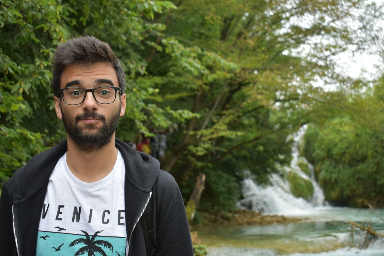 portrait, front view, one person, young adult, real people, casual clothing, water, nature, looking at camera, beard, young men, lifestyles, tree, plant, day, facial hair, focus on foreground, glasses, leisure activity, outdoors, flowing water